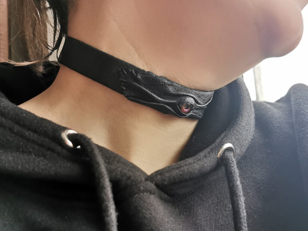 a photograph of a black leather collar, set with a vibrant purple resin eye as though it were a cabochon.